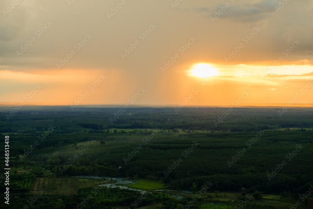 Distant Rainfall in front of the sunset view from wooden bridge on cliff, viewpoint of Wat Phu Thok temple at Bueng Kan province amazing Thailand.