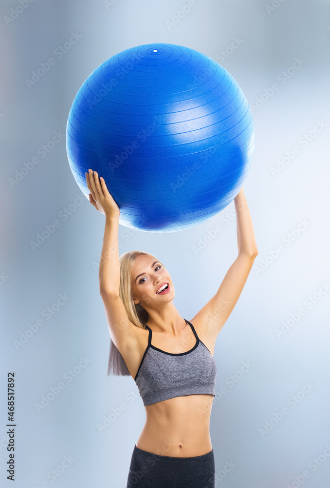 Portrait of happy excited blond young woman in sportswear with fitball, standing over blurred modern gym center background. Fitness, exercising and fit gym concept. Portrait of happy excited blond young woman in sportswear with fitball, standing over blurred modern gym center background. Fitness, exercising and fit gym concept.
