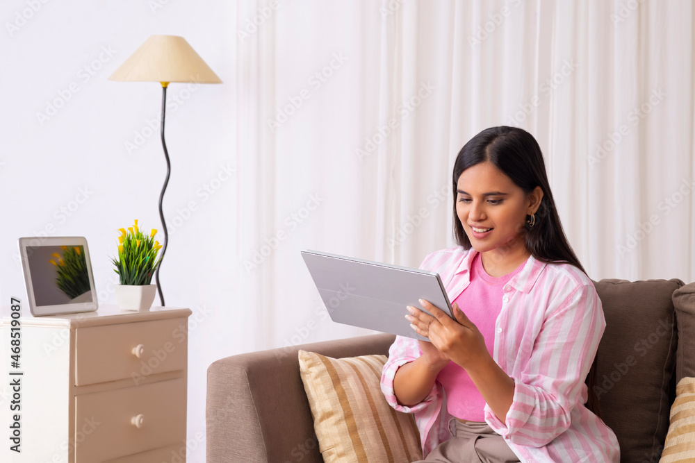 Indian girl looking at her tablet while sitting on sofa Indian girl looking at her tablet while sitting on sofa