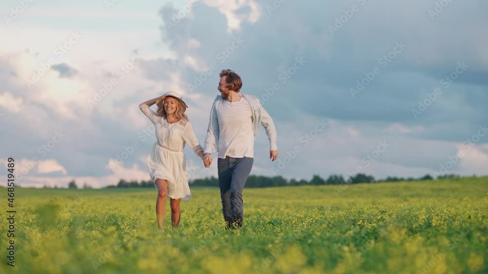 Countryside, cheerful young couple in nature, man and a woman are running through a field of rapeseed holding hands, slow motion. Countryside, cheerful young couple in nature, man and a woman are running through a field of rapeseed holding hands, slow motion.
