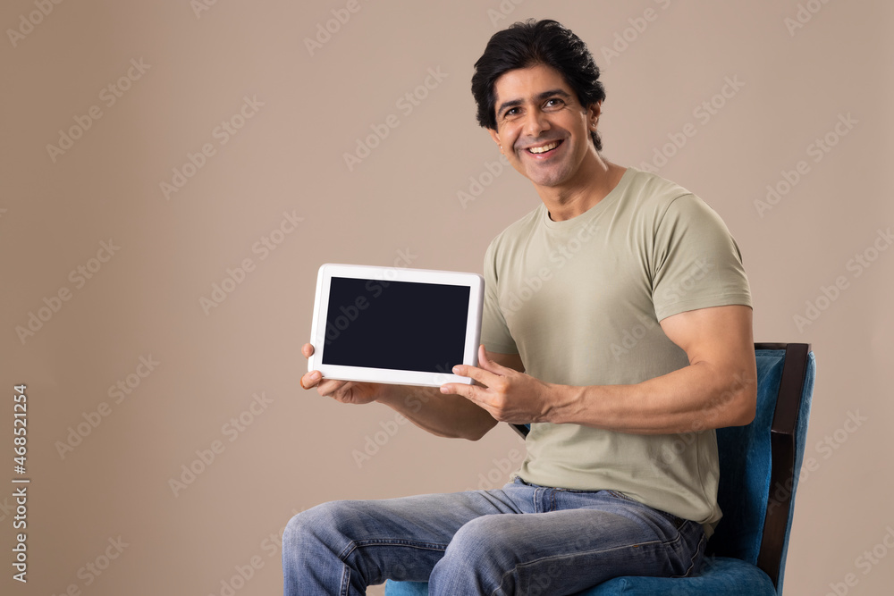 Indian man displaying his tablet while sitting on chair Indian man displaying his tablet while sitting on chair