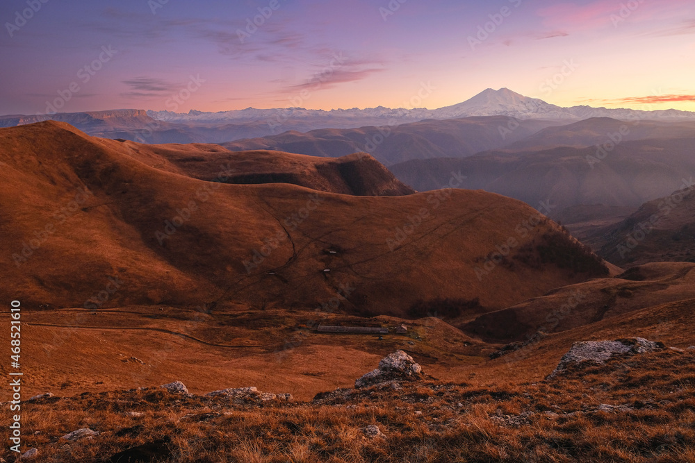 Autumn mountains at sunset. Mount Elbrus in the background. In front of the valley with fog.