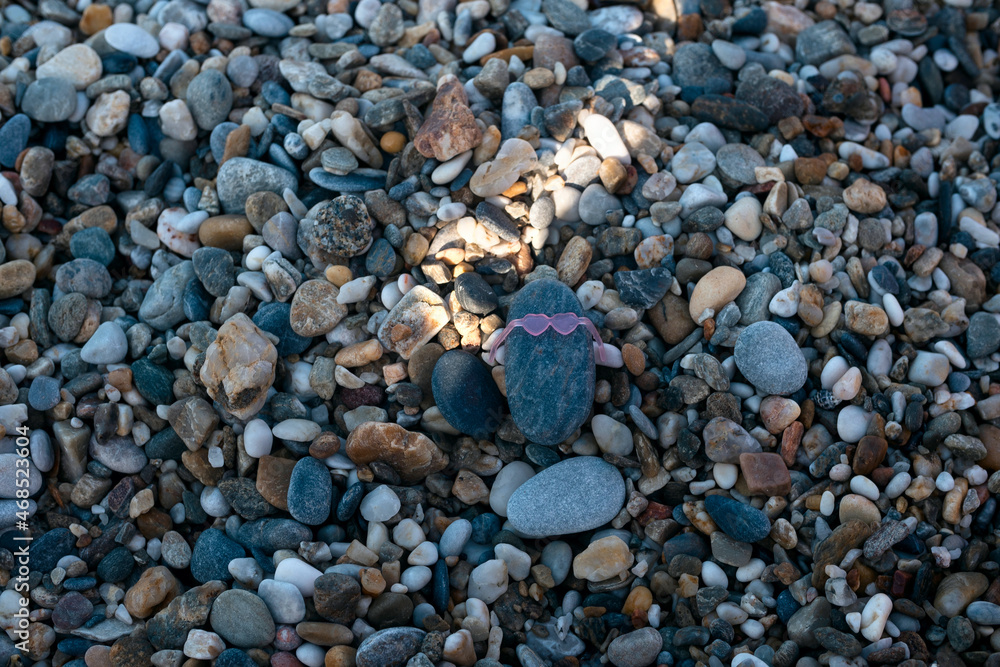 A Pebble stone wearing sunglasses on the pebble beach on summer day. Creativity and playing concept A Pebble stone wearing sunglasses on the pebble beach on summer day. Creativity and playing concept