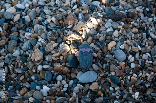 A Pebble stone wearing sunglasses on the pebble beach on summer day. Creativity and playing concept