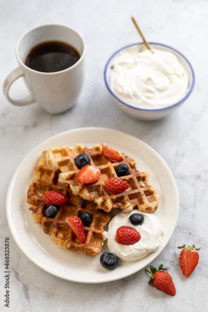 Vertical photo of sweet breakfast: croffles (croissant + waffle) with whipped cream and berries, cup of coffee. Vertical photo of sweet breakfast: croffles (croissant + waffle) with whipped cream and berries, cup of coffee.
