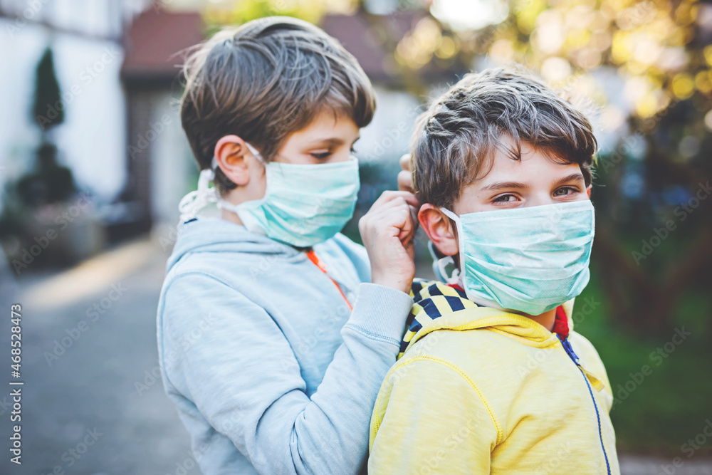 Fototapeta premium Two kids boys in medical mask as protection against pandemic coronavirus disease. Children, lovely siblings and best friends using protective equipment as fight against covid 19.