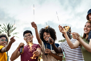 Group of united multiracial friends laughing and celebrating with sparkles outdoors - Young hipster people having fun together with drinks at weekend event party celebration - Friendship concept
