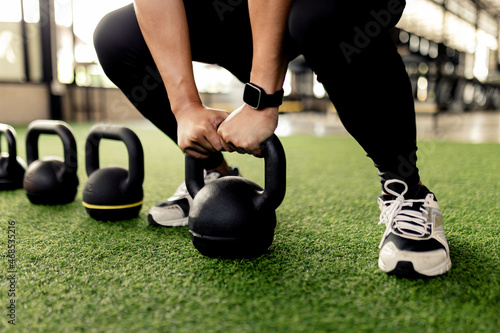 exercise concept The black kettlebells being lined on the green carpet for being done kettlebell swing by someone who wears a grey smartwatch and black pair of shoes