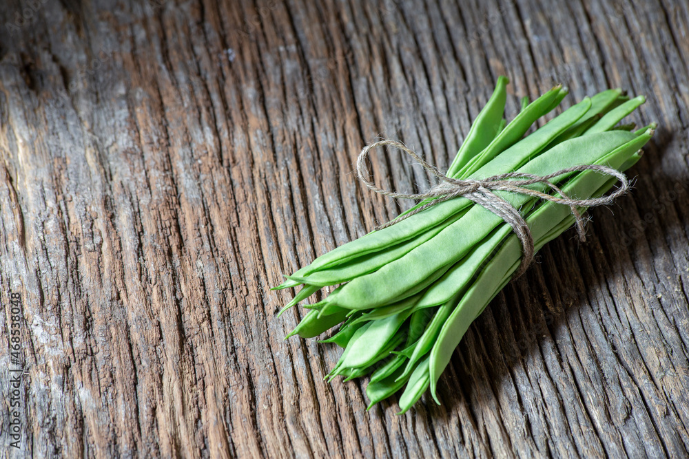 bunch of green flat beans tied with a string on an old wooden plank. sective approach. copy space, text space. horizontal photography.
