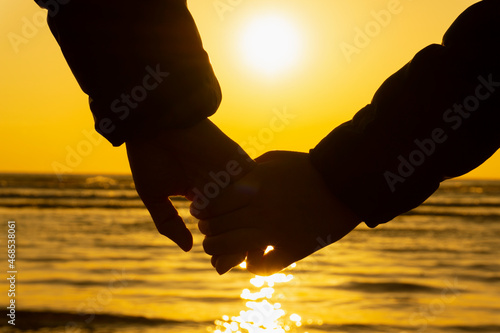Close-up of two people holding hands at the beach in the evening. 夕方の海辺で手をつなぐ二人