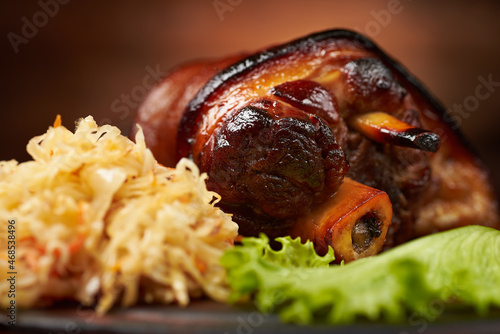 Hot eisbeine (pork knee) with braised sauerkraut cabbage and craft beer on a dark and wooden background. Autumn food concept with copy space. Macro photo with shallow depth of field.