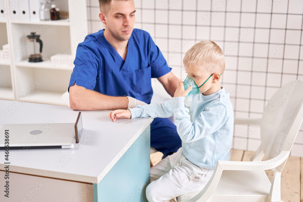 Obraz premium A pediatrician diagnoses lung disease and provides treatment. Breathe the medicine through a nebulizer inhaler.. Portrait of adorable little boy visiting doctor.
