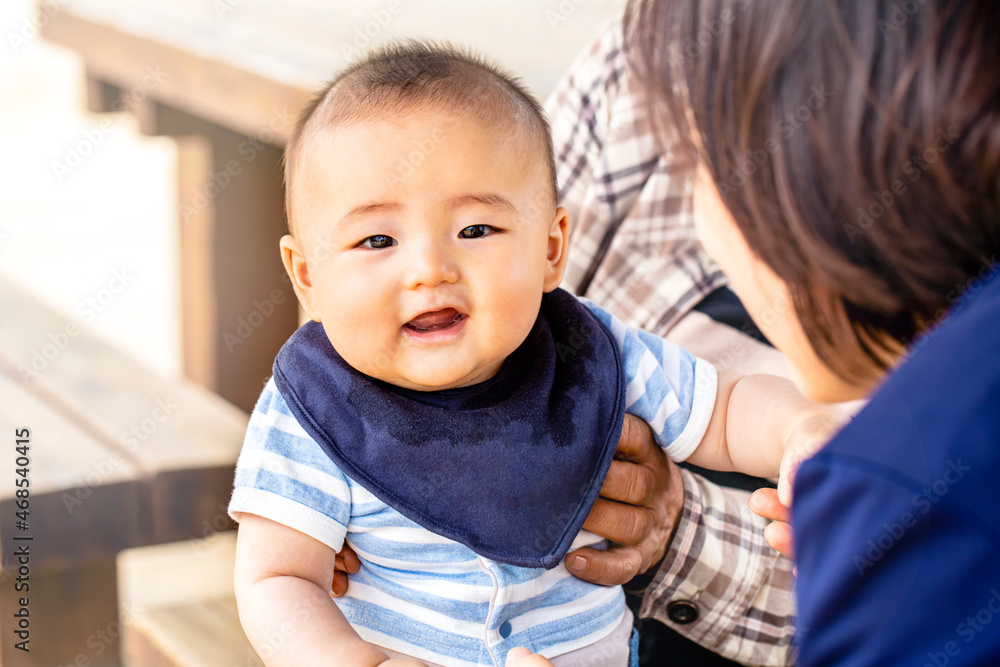 おばあちゃんに抱っこされてお母さんと戯れる赤ちゃんがカメラ目線　3世代が外のベンチに座っている