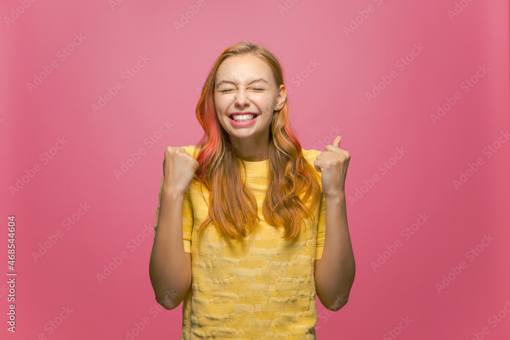Overjoyed lucky young girl winner feeling triumph, rejoicing raising hands with closed eyes from joy on pink background Overjoyed lucky young girl winner feeling triumph, rejoicing raising hands with closed eyes from joy on pink background