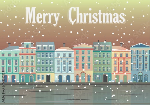 Christmas greetings from at snowy city. House facades in warm soft colors that are reflected in frozen water.
