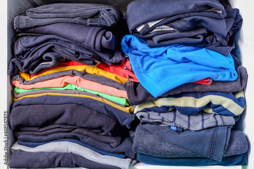 Pile of folded menswear on the shelf. Men's clothing in a closet. Mess in clothes and cleaning of the home cabinet.