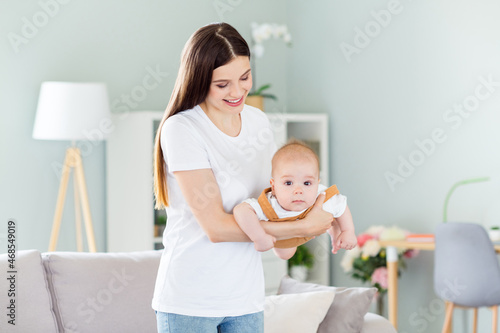 Portrait of attractive careful affecionate cheerful girl playing holding baby enjoying at light home flat indoors
