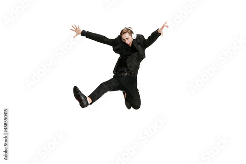 Excited young man in black business suit dancing and listening music isolated on white background. Art, motion, action