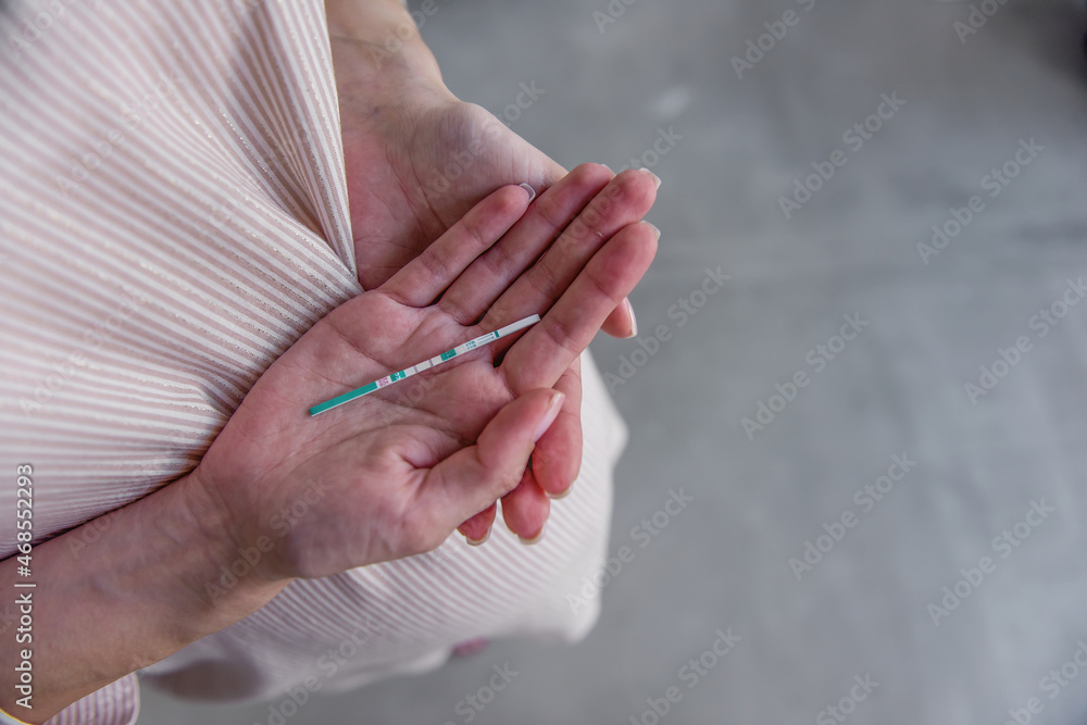 A pregnant young woman is holding a paper pregnancy test, two stripes revealed. Healthy, happy pregnancy. IVF fertilization. Medical treatment of infertility. Surrogacy. Close up, copy space