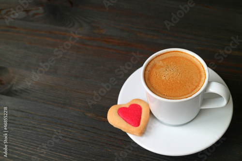 Cup of hot coffee with a heart shaped cookie on black wooden backdrop