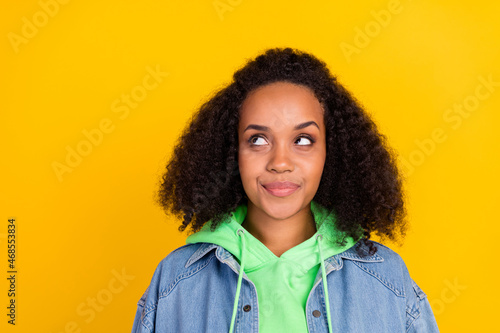 Photo of cute thoughtful african lady dressed jeans green hoodie looking empty space smiling isolated yellow color background © deagreez