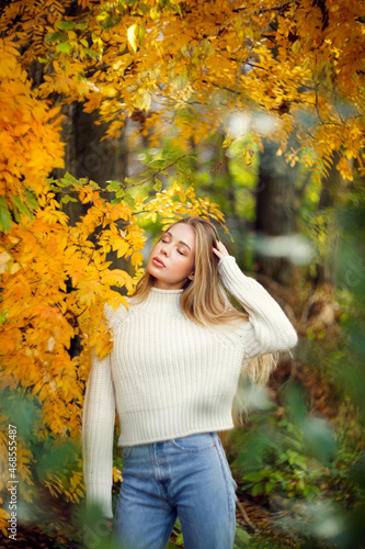 beautiful autumnal young girl in a white sweater in the park among the trees  caucasian girl with beautiful long hair and full lips  portrait of a girl soft focus and beautiful bokeh