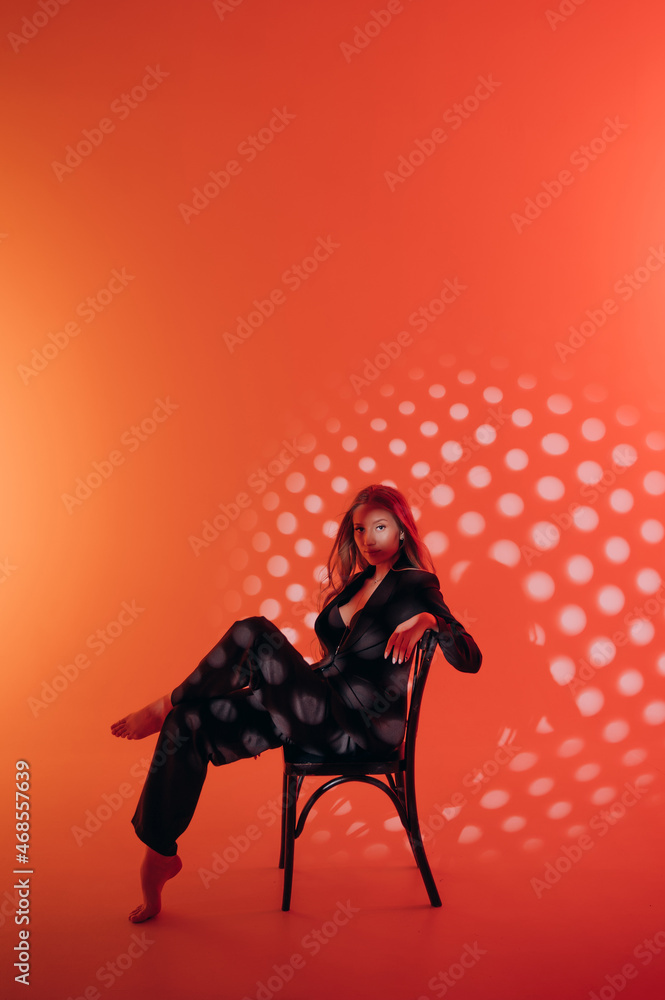 beautiful girl in black suit, blonde hair, red background, photo studio