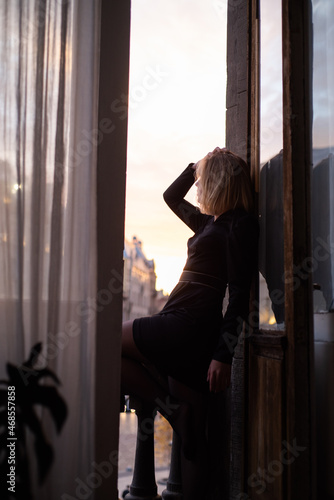 Beautiful young woman near the window on sunset. City view