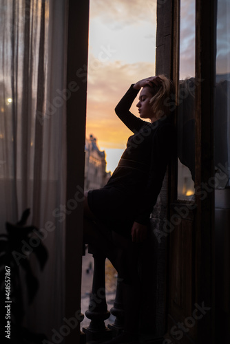 Beautiful young woman near the window on sunset. City view