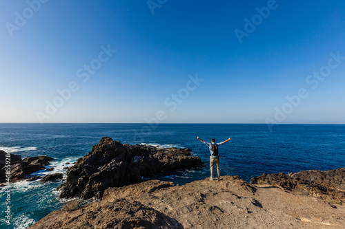 young bright attractive man standing on the ocean and controlling the situation on the beach. Ocean waves and blue sky background