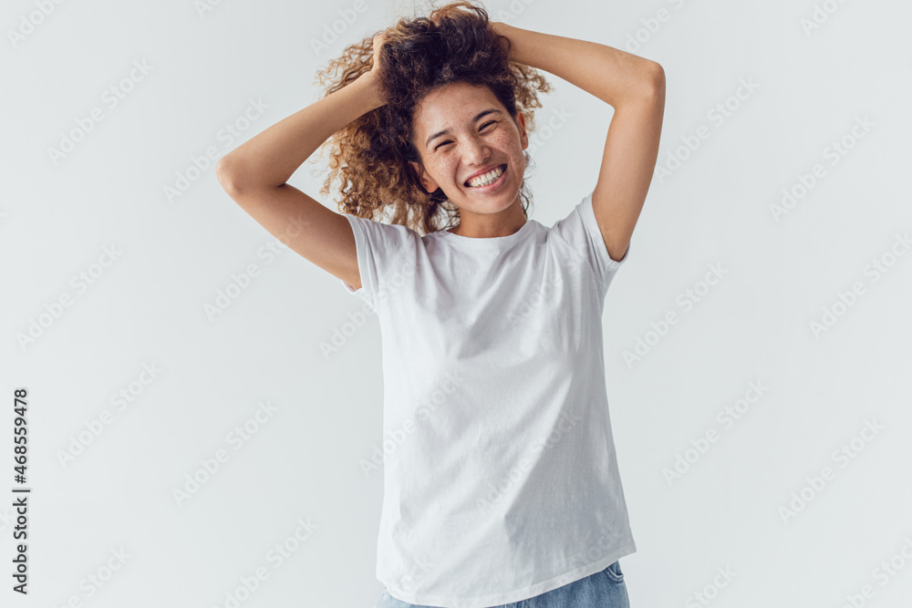 Smiling woman with lush curly hair in white blank t-shirt on a white background. Mock-up. Smiling woman with lush curly hair in white blank t-shirt on a white background. Mock-up.