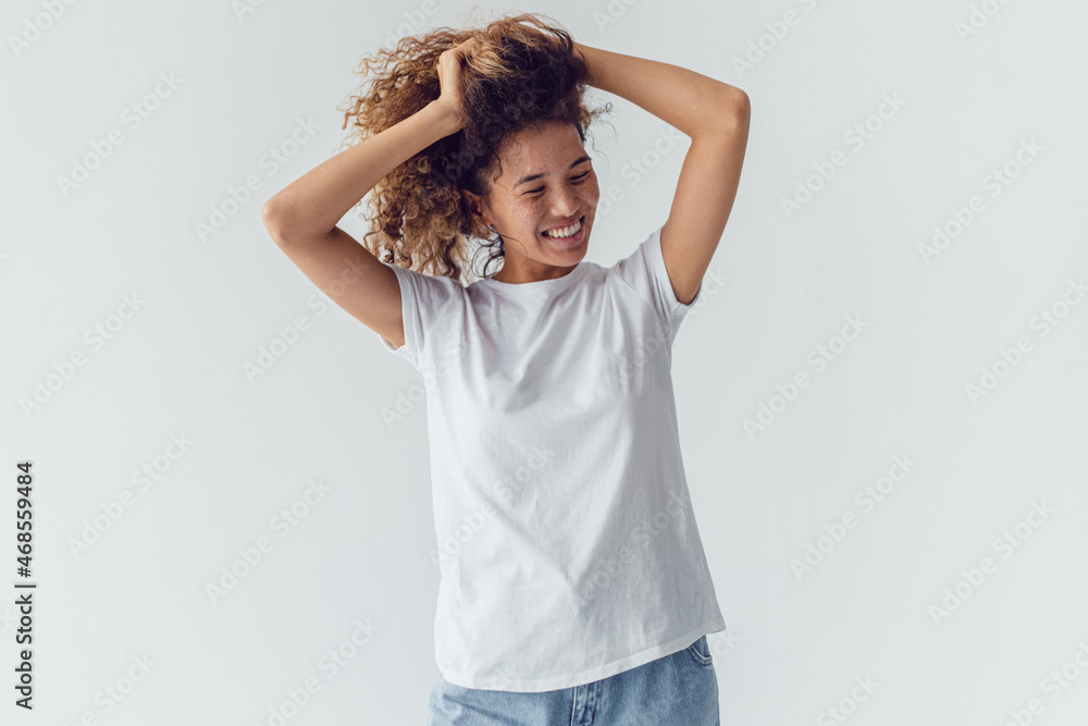Smiling woman with lush curly hair in white blank t-shirt on a white background. Mock-up. Smiling woman with lush curly hair in white blank t-shirt on a white background. Mock-up.