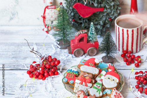 Christmas cookies in a plate with festive decorations and mug with cocoa drink on the table decorated with toys, rowan berries, winter holiday dessert concept, copy space 
