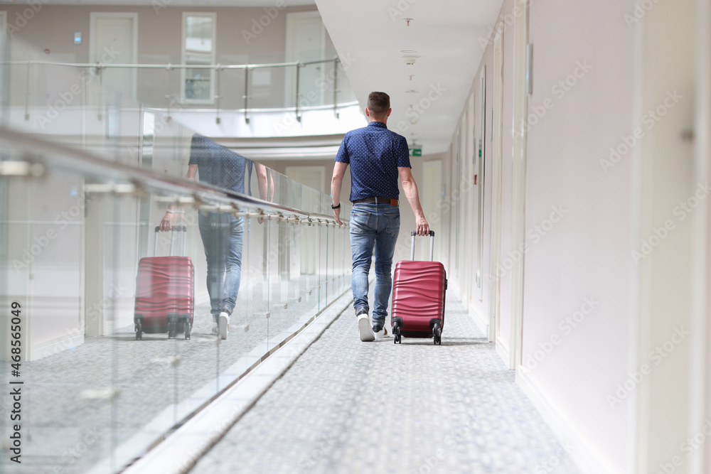 Man with suitcase walking down in hotel corridor back view