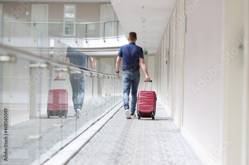 Man with suitcase walking down in hotel corridor back view