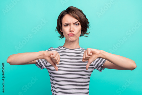 Photo of young girl unhappy upset show thumb-down bad quality dislike isolated over teal color background photo