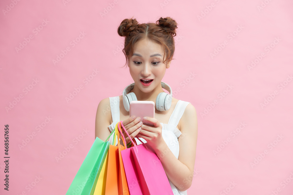 young excited cheerful woman holding shopping bags isolated over pink background using mobile phone young excited cheerful woman holding shopping bags isolated over pink background using mobile phone
