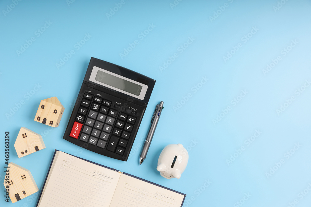 Top view LOAN on the black calculator with little home models, notebook, and white piggy bank on blue background with copy space. Concept saving money for investment business property. Top view LOAN on the black calculator with little home models, notebook, and white piggy bank on blue background with copy space. Concept saving money for investment business property.