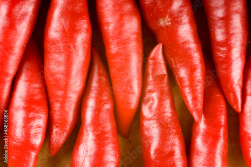 Bunch of red chilli peppers sitting end to end on a timber chopping board