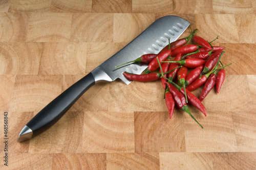 Bunch of red chilli peppers on a timber chopping board with a silver knife
