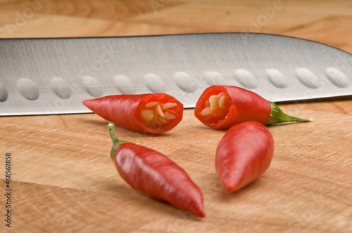 Four red chilli peppers one cut in half on a chopping board with a silver knife