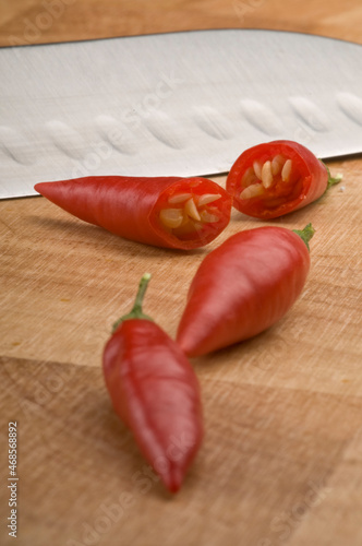 Four red chilli peppers one cut in half on a chopping board with a silver knife