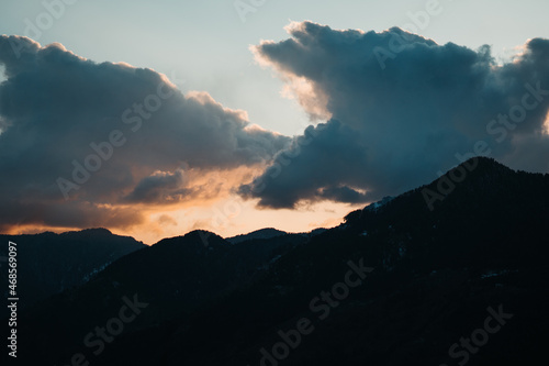 Orange clouds above the snow covered mountains of Kullu Valley during the sunset at Kullu in Himachal Pradesh, India. Beautiful sunset above the mountains besides Kullu in Himachal Pradesh, India.
