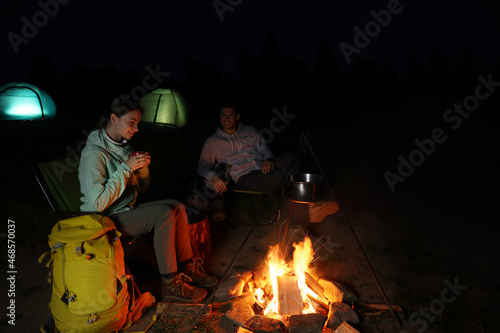Couple sitting near bonfire in camp at night