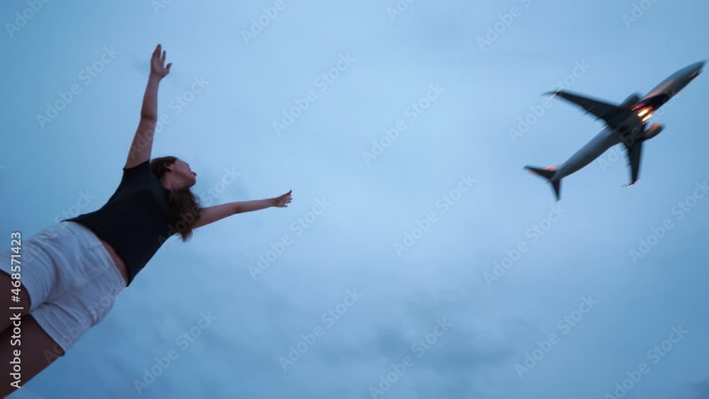 Excited tourist woman stand with hands raised up to flying by airliner, low angle shot. Aircraft pass low over, just take off from airport runway. Late evening time, cloudy and dim sky on background Excited tourist woman stand with hands raised up to flying by airliner, low angle shot. Aircraft pass low over, just take off from airport runway. Late evening time, cloudy and dim sky on background