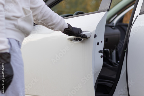 A man in a white sweater and black gloves opens the car door to steal him on a warm autumn day. Selective focus. Close-up