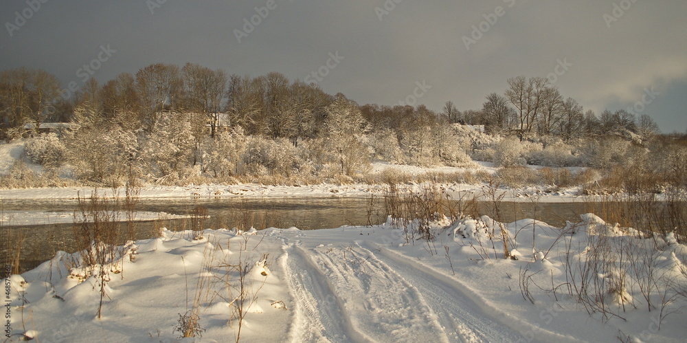 River Venta, snowy shore and car wheel tracks on a sunny winter day, Kuldiga, Latvia.