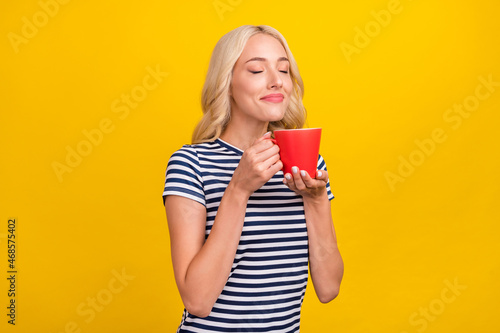 Portrait of attractive dreamy cheerful girl drinking smelling latte good morning isolated over shine yellow color background