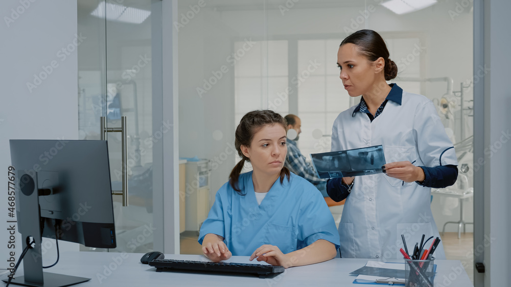 Fototapeta premium Team of nurse and stomatologist examining x ray and computer screen for professional oral care operation at dental clinic. Orthodontic staff using technology for modern radiography