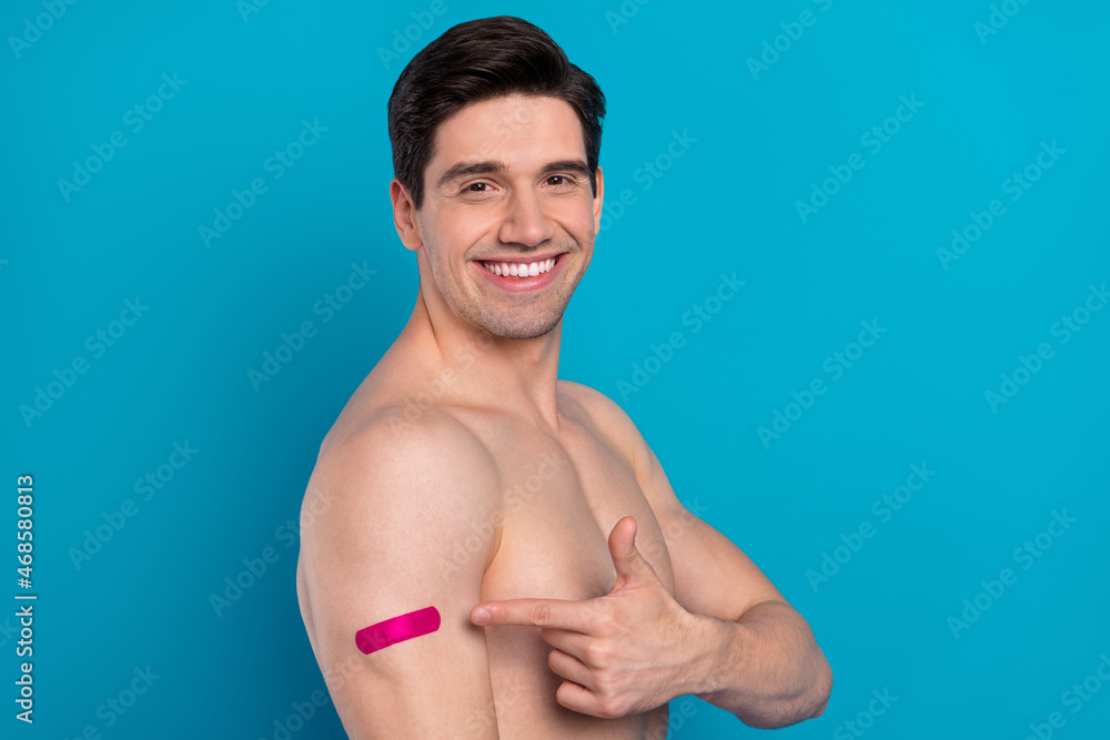 Photo of charming cheerful young guy topless smiling pointing finger vaccination patch isolated blue color background